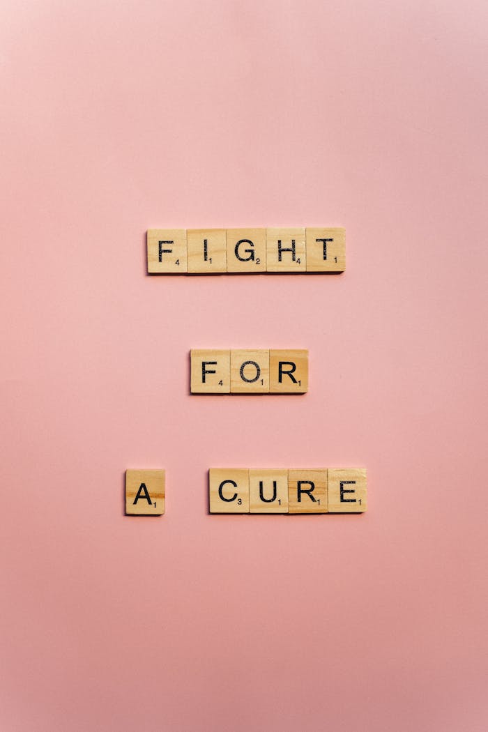 Wooden letter blocks spell 'Fight for a Cure' on a pink background promoting cancer awareness.